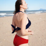 ShowBee SwimIt bikini briefs in fire red with golden rings, combined with the SwimIt bikini top in navy blue color, decorated with silver rings. View from the side.