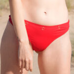 ShowBee SwimIt bikini tanga in fire red, decorated with golden rings. Front view.